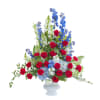 Tall arrangement of red roses, blue delphinium, and white flowers in a white vase