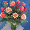 Tall arrangement of coral and orange roses in a clear glass vase on a small wooden table