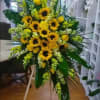 A STANDING EASEL WITH TROPICAL LEAFS, YELLOW ROSES, SNAPSDRAGONS AND SUNFLOWERS (STANDS