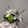 White lilies and roses arranged in a white vase with green accents