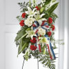 Standing floral spray with white lilies, red carnations, and ribbon on an easel