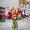 Mixed bouquet of roses, gerbera daisies, and pink blooms in a clear glass vase