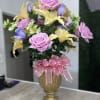 Pink and yellow floral arrangement in a gold vase with a pink ribbon bow