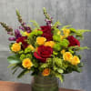 Red and yellow roses arranged in a glass vase with purple spikes