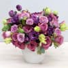 Compact arrangement of purple and pink roses with lisianthus and tulips in a white pot