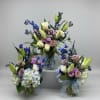 Three pastel floral arrangements in glass vases with blue ribbon bows
