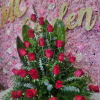 Red rose arrangement against a pink floral wall with gold lettering