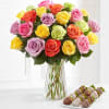 Colorful rose bouquet in a clear glass vase with chocolate-covered strawberries beside it