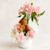 Pink lilies and carnations arranged with a teddy bear in a white vase