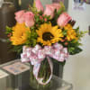 Pink roses and sunflowers in a glass vase with a floral ribbon