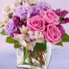 Pink roses and purple flowers arranged in a clear square vase