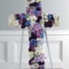 Floral cross arrangement in purple, blue, and white flowers on a stand