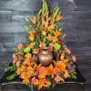Orange lilies and roses arranged around a bronze urn centerpiece