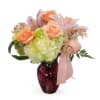Bouquet of peach roses and hydrangeas in a red glass vase with a pink ribbon
