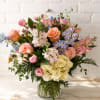 Mixed bouquet of pink, peach, lavender, and white flowers in a glass vase