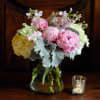 Pink peonies and pale hydrangeas in a glass vase with a small candle beside it