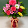 Pink roses and lilies arranged in a red vase with a ribbon