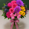 Colorful bouquet of roses, chrysanthemums, carnations, and alstroemeria in a glass vase with a pink ribbon