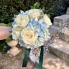 Handheld bouquet of white roses and pale blue hydrangeas with green ribbon