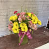 Bouquet of yellow daisies and pink alstroemeria in a green vase with a pink polka-dot ribbon