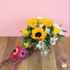 Yellow sunflowers and white flowers in a silver vase with loose blooms beside it.