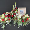 Patriotic red and white floral display with urn and framed flag photo against a black background