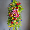 Tall standing floral spray with pink lilies, red roses, and bright mixed blooms