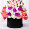 Pink-tipped roses, purple orchids, and white flowers in a black hat box