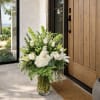 Tall white floral arrangement in a glass vase by a wooden door