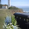 White and blue funeral flowers beside a black casket outdoors