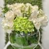 Low arrangement of white roses and green hydrangea in a round glass bowl vase