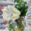 Round glass vase with white roses and hydrangeas, tall greenery, and seashells with a small yellow duck in the water