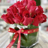 Compact arrangement of red roses in a clear glass cube vase with a red printed ribbon