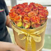 Round gold box of orange and yellow roses tied with a gold satin ribbon.