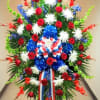 Patriotic standing spray of red roses, white mums, and blue accents with striped bow on an easel