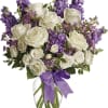 White roses and purple flowers in a glass vase with a purple ribbon