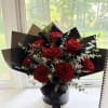 Red roses arranged in a black hatbox with black wrapping and ribbon