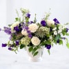White roses and purple bellflowers arranged in a white vase