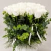 White roses arranged in a round white vase with lush greenery and ribbon accents