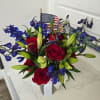 Red roses and blue flowers in a clear vase with an American flag