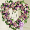 Heart-shaped floral wreath on an easel with pink, white, and purple flowers