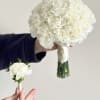 White carnation bouquet and matching boutonniere held against a plain background