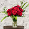 Red roses arranged in a clear glass vase with fern accents