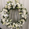 White floral wreath on a black stand with roses and lilies