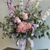 Tall pink and white floral arrangement in a glass vase with a ribbon