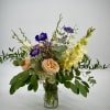 Mixed bouquet in a clear glass vase with peach roses and purple blooms