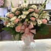 Pink and white mixed flower arrangement in a white pedestal vase with a pink bow
