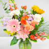 Mixed bouquet of pink, orange, yellow, and white flowers in a glass vase