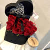 Red roses arranged in a black heart-shaped box with a ribbon and wicker heart topper
