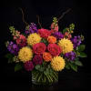 Mixed bouquet of roses, dahlias, and purple accent flowers in a glass vase
